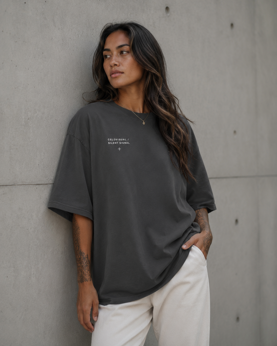 Person wearing a dark gray oversized t-shirt with text, standing against a concrete wall.