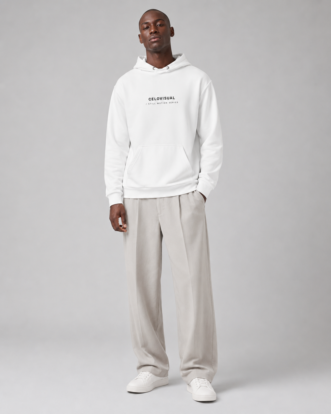 Man wearing a white hoodie with text and light gray pants on a gray background