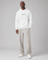 Man wearing a white hoodie with text and light gray pants on a gray background