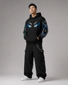Person wearing a black hoodie with eye designs and black pants on a gray background