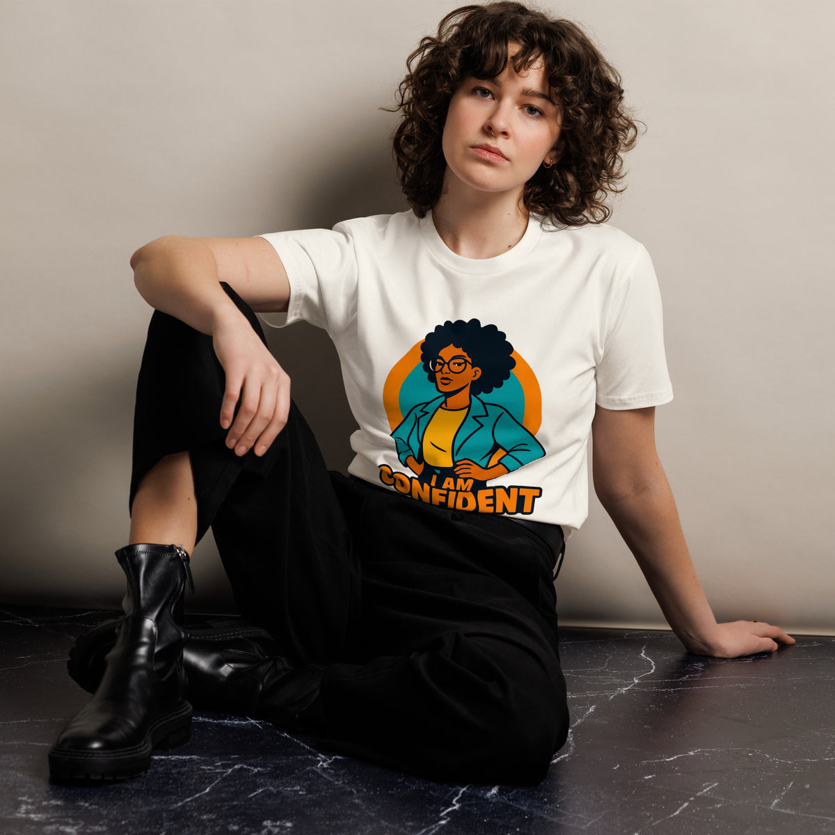 Person wearing a white t-shirt with a colorful graphic design sitting on a dark surface.
