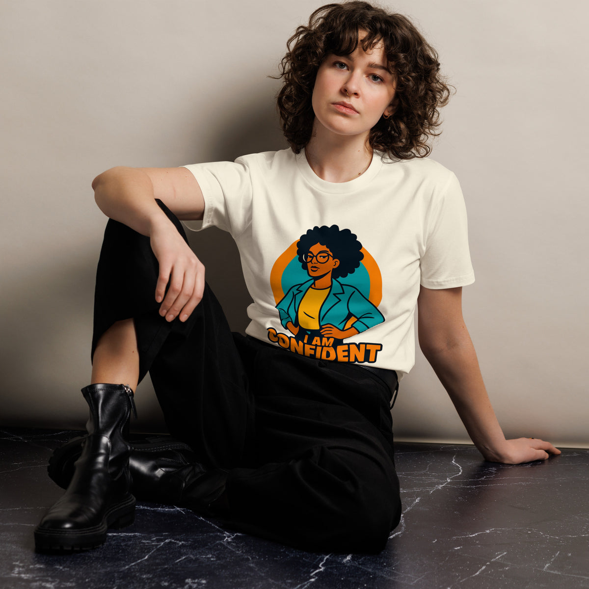 Person wearing a white t-shirt with a colorful graphic design sitting on a dark surface.